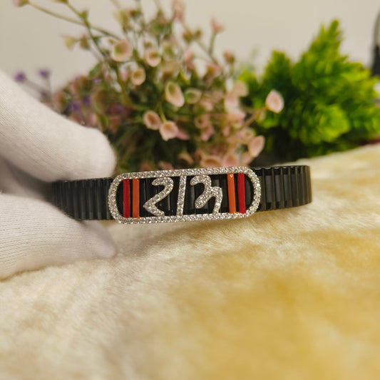 A black pleated bracelet with a central rectangular plate featuring the number 23 in silver with clear rhinestones, flanked by red and black stripes, held by a white-gloved hand against a soft beige background with blurred flowers.