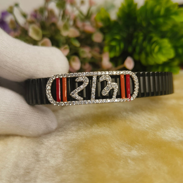 A black bangle bracelet with a rectangular silver-toned bezel set with clear stones, featuring red and black striped inlays and silver Devanagari numerals, held by a white-gloved hand.